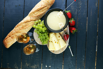Gourmet Swiss fondue dinner with assorted cheeses on a board and strawberries alongside a heated...
