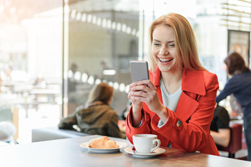 Cheerful blond woman using smartphone in cafeteria