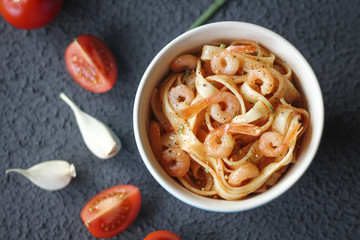Italian tagliatelle pasta with shrimps and tomato sauce on dark background.