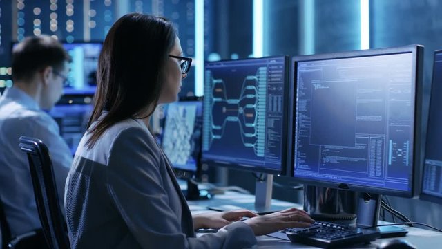  Female Engineer Controller Observes Working of the System. In the Background People Working and Monitors Show Various Information. Shot on RED EPIC-W 8K Helium Cinema Camera.