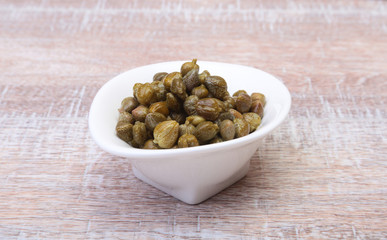 bowl with fresh capers on wooden table