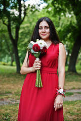 Cute girl bridesmaid at red dress with wedding bouquet at hand.