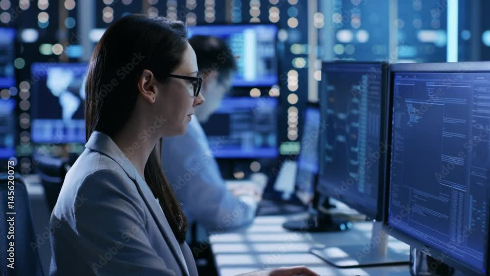 Poster close-up footage of female it engineer working in monitoring room. she works with multiple displays.