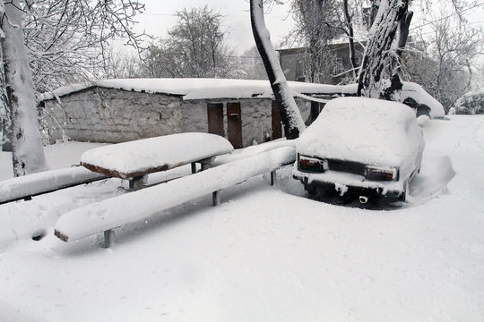 The car is covered with snow. Big snow covered the earth, buildings, roofs and transport