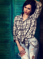 Beautiful makeup woman in trendy black and white checkered shirt and blue ripped jeans thinking and looking down on blue wooden background. Short hairstyle. contrast portrait. Toned fashion portrait