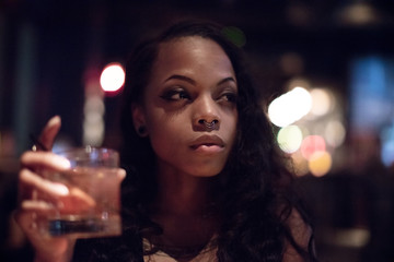 A young, black woman enjoys a drink at a Cocktail Lounge. Shot late night on a Spring 2017 evening.