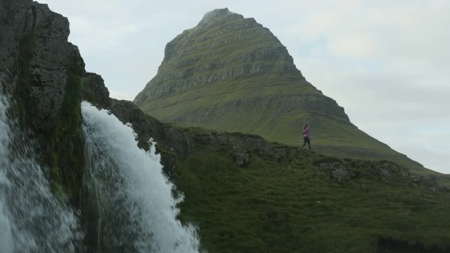 Woman running down hill near Kirkjufell waterfall in Iceland