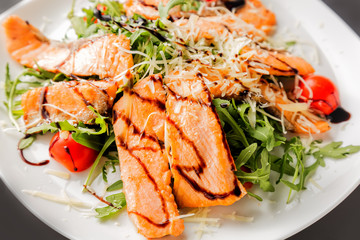 Fresh salad of salmon pieces, cherry tomatoes, lettuce, cheese and sauce on a white plate close up