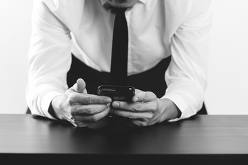 close up of businessman working with smart phone on wooden desk in modern office,black and white
