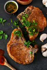 Juicy grilled pork steak with pesto sauce and tomato sauce on a black background