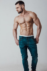 Muscle male model with muscular body in jeans posing on grey background. Studio shoot.