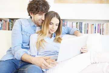 Spend time together. Shot of a smiling young woman and an affectionate handsome man relaxing at home and using laptop. 