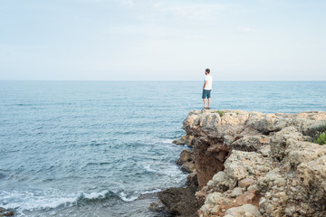 Fototapeta na wymiar hombre joven de pie sobre un acantilado al atardecer. Mar Mediterráneo