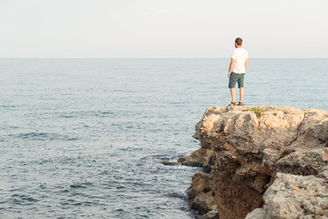 Hombre joven de pie sobre un acantilado al atardecer. Mar Mediterráneo