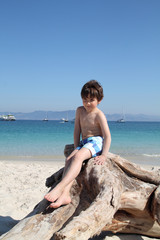 child sitting in a diftwood in the beach