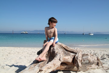 kid sitting in a driftwood in the beach