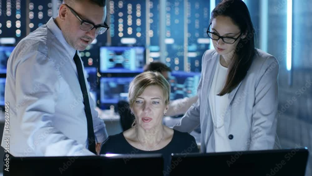 Poster Team of System Analysts Have Discussion on Monitoring Room. In the Background People Working with Multiple Displays Showing Useful Data. Shot on RED EPIC-W 8K Helium Cinema Camera.