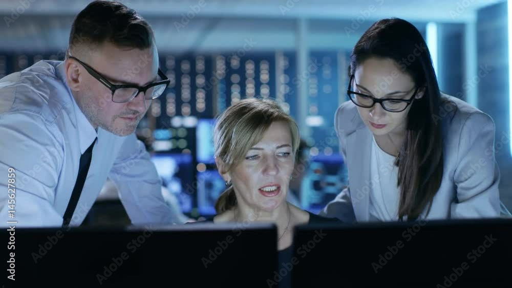 Poster Team of System Technicians Have Discussion on Monitoring Room. In the Background People Working with Multiple Displays Showing Useful Data. Shot on RED EPIC-W 8K Helium Cinema Camera.