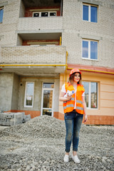 Engineer builder woman in uniform waistcoat and orange protective helmet hold business drawing paper roll against new building. Property living block theme.