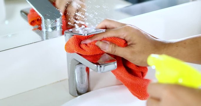 Video footage of housemaid hands using a spray detergent to clean faucet and sink in the bathroom at home. Professional shot in 4K resolution