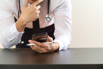 close up of smart medical doctor working with smart phone and stethoscope on dark wooden desk