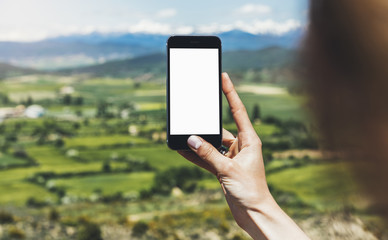 Hipster photograph on smart phone gadget mobile, mock up of blank screen. Traveler hold and using in hand mobile on background mountain landscape horizon. Tourist look map on trip, lifestyle concept