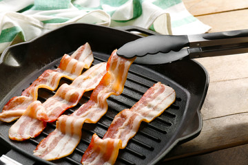 Placing bacon slice in pan with tongs, closeup
