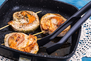 Fried meat on skewers in frying pan, blue background