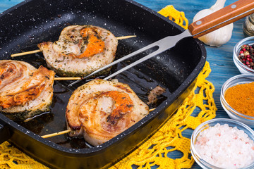 Fried meat on skewers in frying pan, blue background