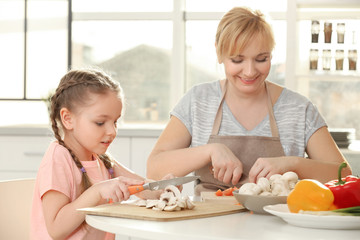 Little girl and her grandmother cooking in kitchen