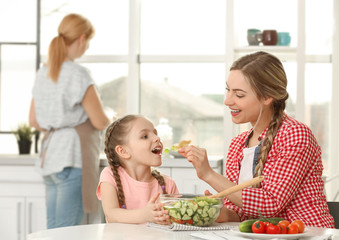 Young woman with her daughter eating salad in kitchen