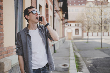 Happy young hipster man walking on the street and talking on phone