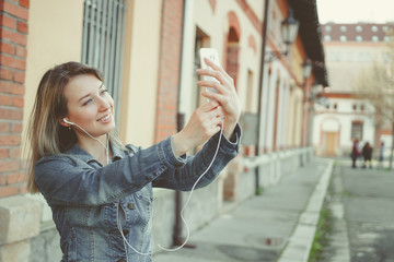Happy young woman walking on the street, making selfie with her smartphone