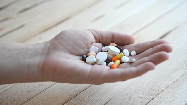 Many different pills fall into a person's hand