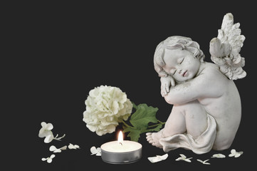 Angel, candle and white flower on dark background