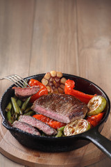 Beef steak with vegetables on a cast-iron frying pan. Copy space, selective focus.