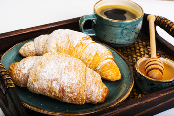 Croissant, honey and espresso in blue vintage bowl on wooden tra