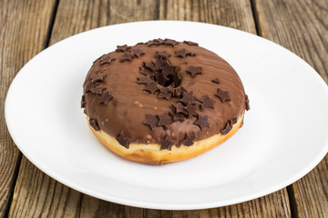 One donut in chocolate glaze on wooden background
