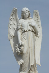 Gravestone memorial with angel holding wreath of flowers against overcast sky