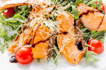Fresh salad of salmon pieces, cherry tomatoes, lettuce, cheese and sauce on a white plate close up