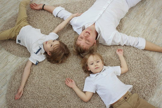 Top view of young father with cute little sons lying on floor