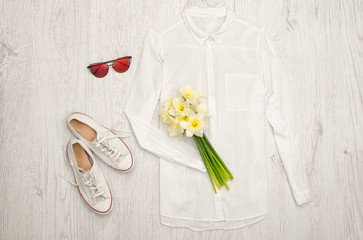 White shirt, glasses, sneakers and a bouquet of daffodils. Wooden background. Fashionable concept