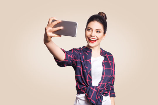 Young beautiful happy woman in casual style holding phone and doing selfie with smart phone. studio shot on beige background.