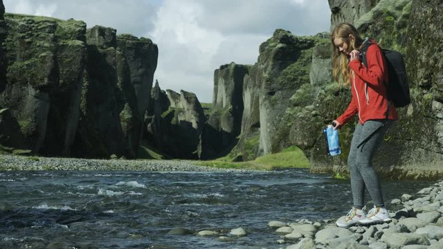 Woman hiker stops to fill up water bottle in river