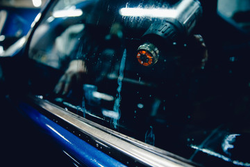 Master installs a tint film for the car glass with a hairdryer and spatula with glare of light. Concept tinting car