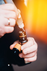 Close-up of a man dripping a fragrant liquid on a cotton wool electronic cigarette. Nichrome heated. The concept of safe replacement of cigarettes and tobacco.