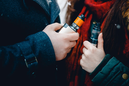 Close-up of a man and a girl are smoking electronic cigarettes wape mod and drip. There are clubs of steam. Concept of smoking in public places is steam and smoke.