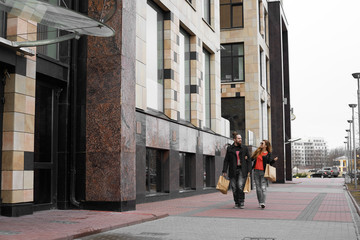 Happy family come home after shopping in modern street. Stylish beard man and his girl friend going with paper package after visit favorite shop. Weekend for a lovers couple in big city.