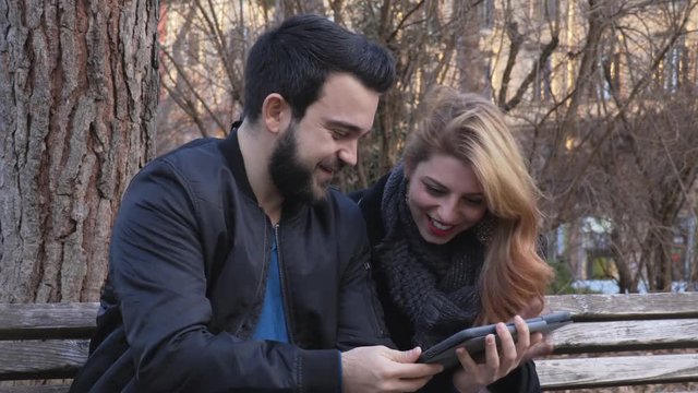 Portrait of amusing,smiling couple on the bench looking at photos on the tablet