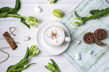 Coffee cappuccino with cinnamon, macaron, marshmallow and beautiful spring tulips on white background